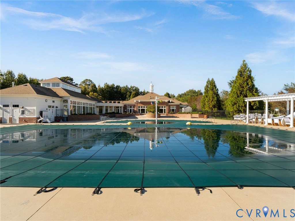 Outdoor swimming pool with a secured safety cover, concrete decking, and a white architectural pergola