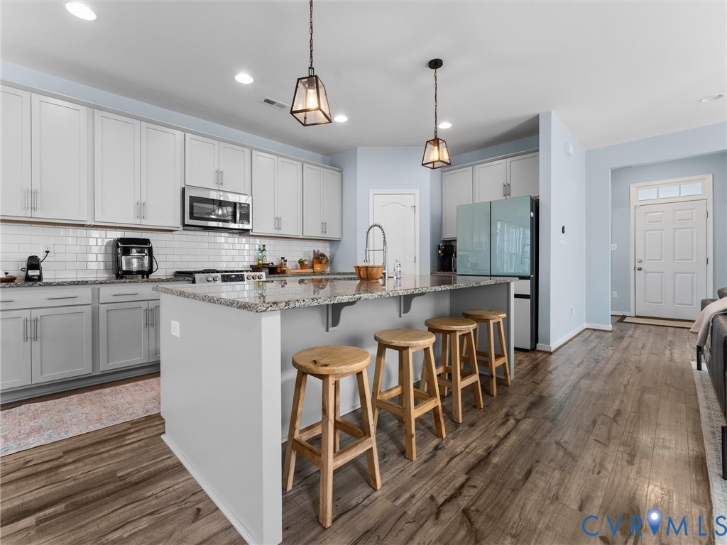 Kitchen featuring white shaker cabinetry, stone countertops, subway tile backsplash, a center island with pendant lighting, and wood-finish flooring