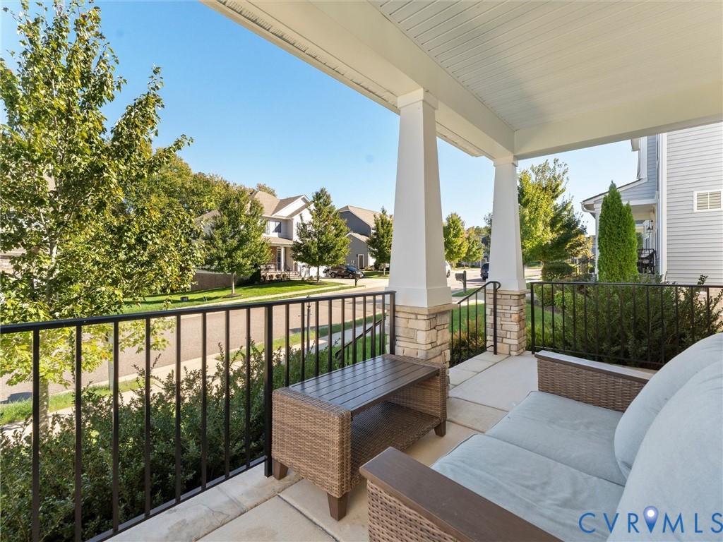 Covered front porch featuring tapered columns with stone-veneer bases, metal railings, and a concrete floor
