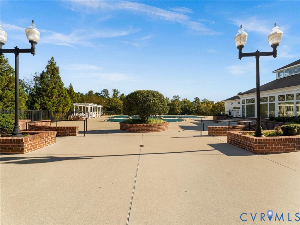 Concrete pool deck featuring brick-encased planters, dual-head iron lamp posts, and a covered pavilion