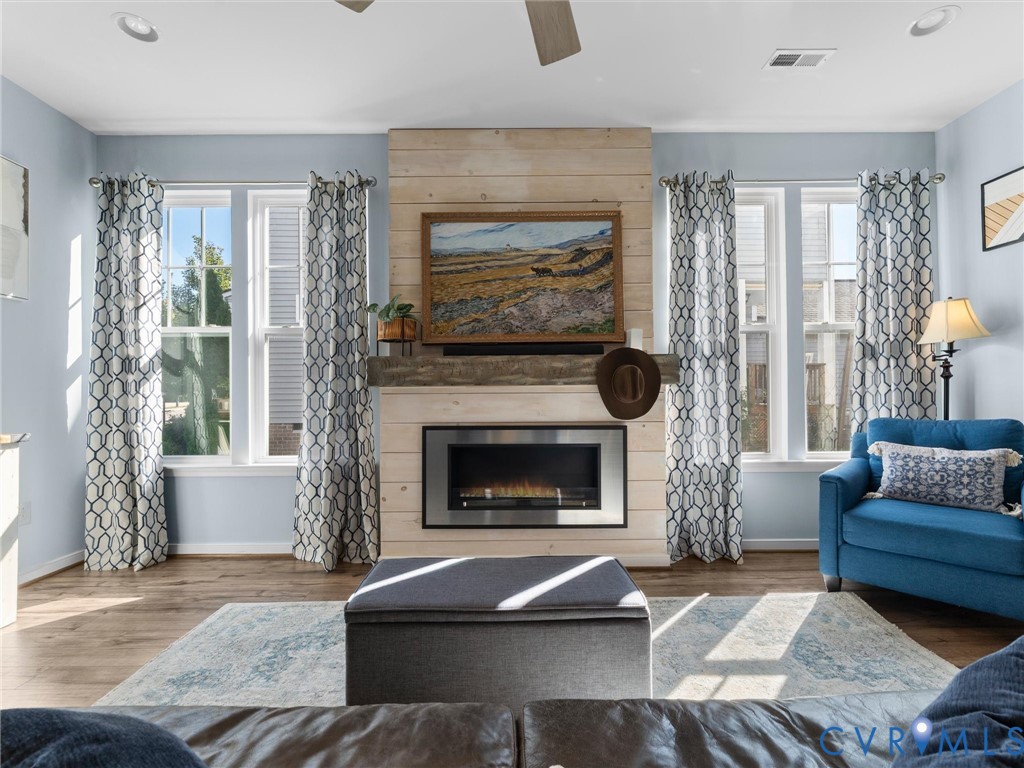 Fireplace with a horizontal wood-plank surround and substantial timber mantel, wood-finish flooring, recessed lighting, and multiple tall windows