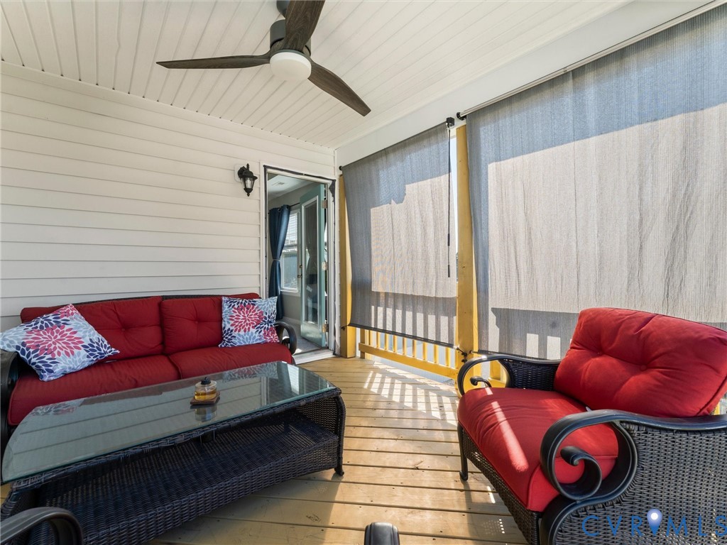 Covered porch featuring wood-finish decking, horizontal siding, a ceiling-mounted fan with integrated lighting, and retractable exterior shades