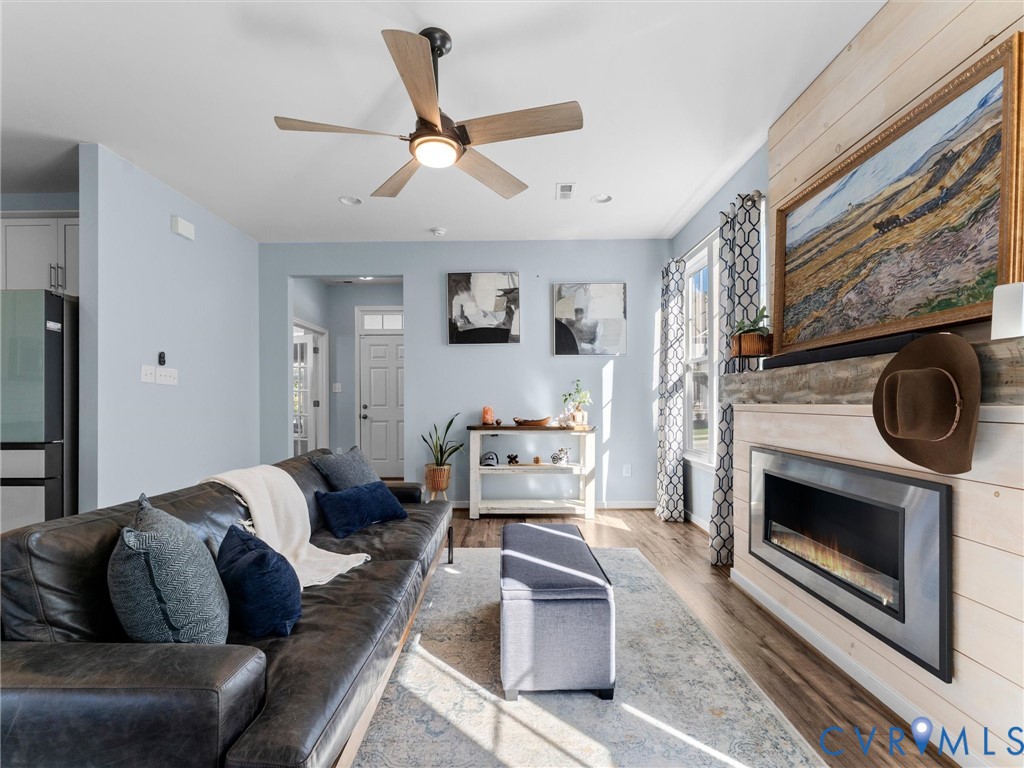 Living space featuring horizontal wood-plank wall detailing, a built-in electric fireplace with a stone-texture hearth, wood-finish flooring, and a ceiling fan with integrated lighting