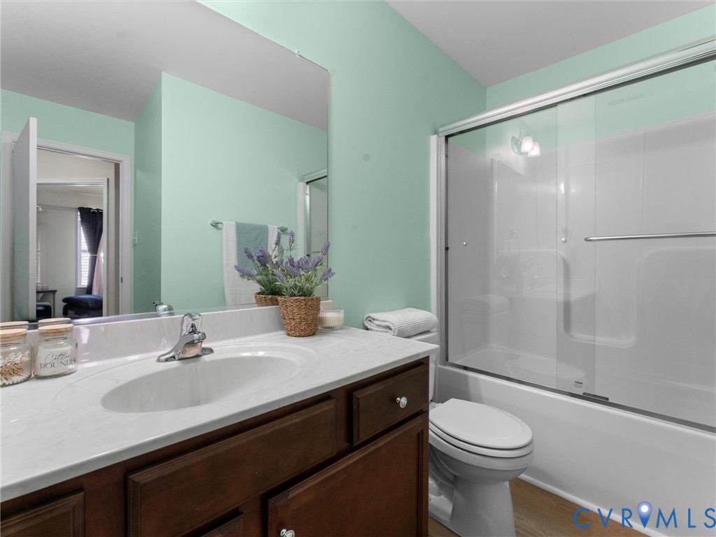 Bathroom featuring a vanity with a light-toned countertop, integrated oval sink, chrome-finish faucet, and a glass-enclosed tub-shower combination