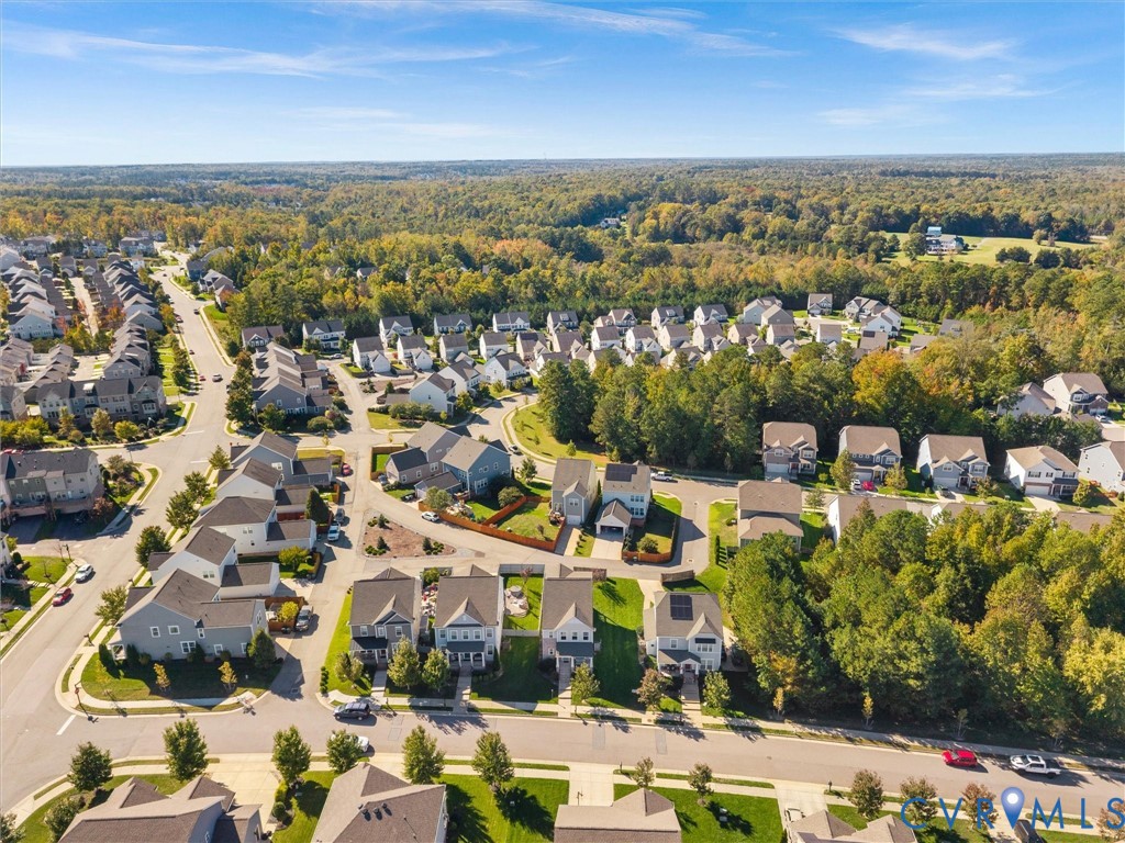 Aerial perspective of a residential community featuring multi-story dwellings, paved roadways, sidewalk infrastructure, and extensive forested canopy