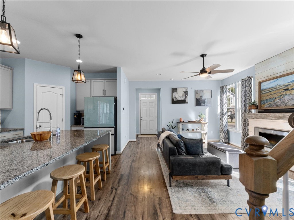 Open-concept kitchen featuring an expansive stone-topped island, wood-finish flooring, a fireplace with horizontal shiplap surround, and suspended pendant lighting