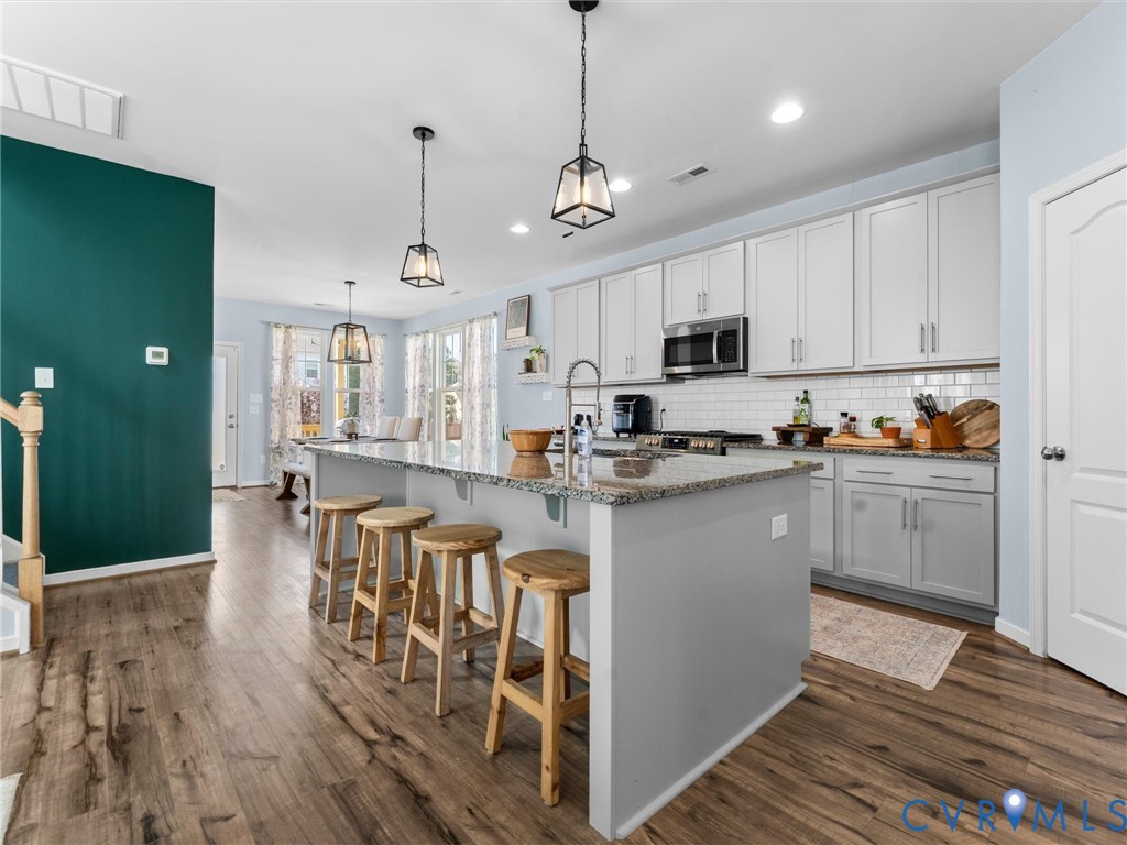 Kitchen featuring wood-finish flooring, a stone-topped island, white shaker-style cabinetry, a white subway tile backsplash, and decorative pendant lighting