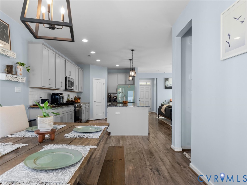 Kitchen featuring white shaker-style cabinetry, a central island with a stone countertop, wood-finish flooring, recessed lighting, and a geometric metal chandelier