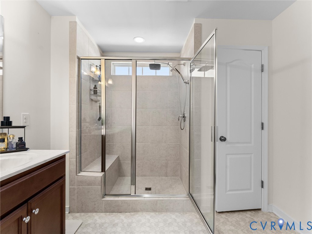 Walk-in shower featuring a built-in tiled bench, glass enclosure, and rainfall showerhead, accompanied by a wood-finish vanity cabinet