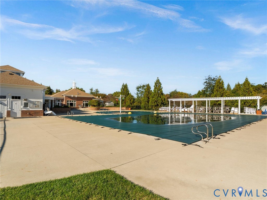 Outdoor swimming pool with a safety cover, concrete decking, metal railings, and a wooden pergola structure
