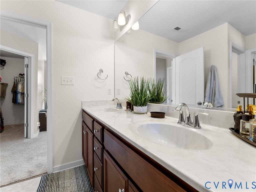 Bathroom vanity featuring a light-toned stone-finish countertop, dual under-mount sinks, polished chrome faucets, and stained wood cabinetry