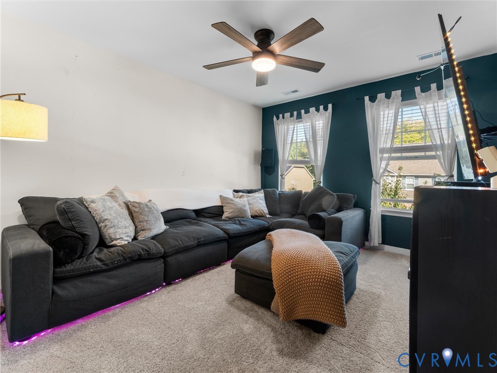 Dual-tone wall finishes featuring a deep accent wall, neutral carpeting, and a multi-blade ceiling fan with integrated lighting
