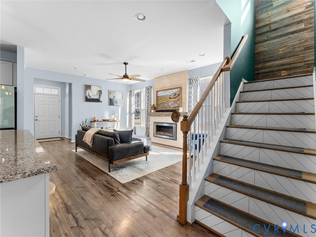 Open-concept floor plan featuring wood-finish flooring, staircase with geometric-patterned risers, wood-paneled accent wall, and fireplace with a wood-plank surround