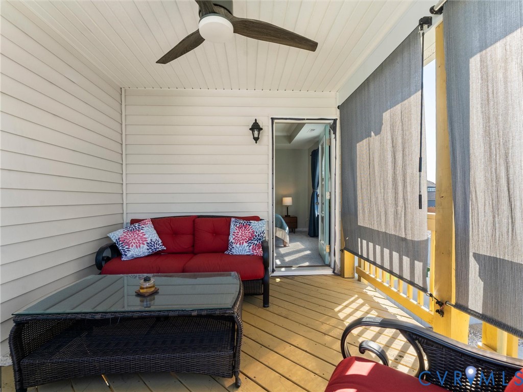 Covered balcony featuring horizontal lap siding, beadboard ceiling, ceiling fan with integrated lighting, wall-mounted lantern-style sconce, and wood-finish decking