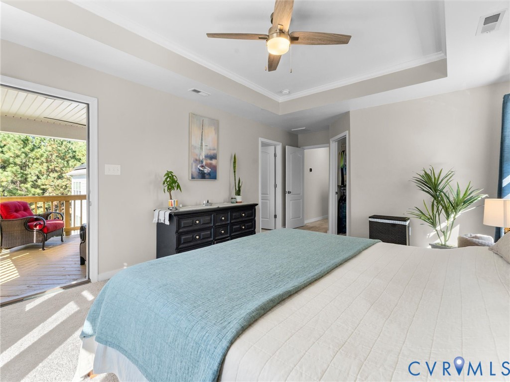 Tray ceiling featuring a central ceiling fan, neutral wall color, and glass-paned door opening to a wooden deck