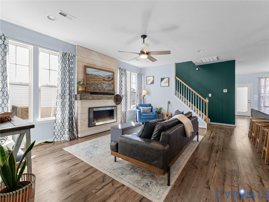 Wood-finish flooring, fireplace with horizontal wood-plank accent wall, ceiling fan, and staircase with wooden handrail