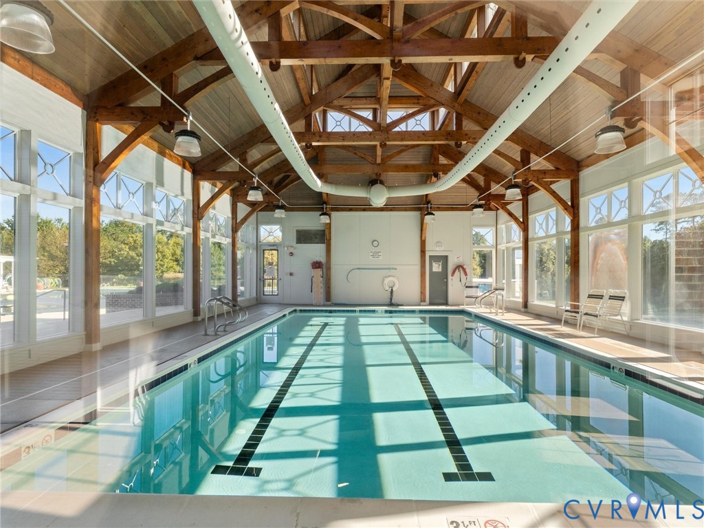 Indoor pool facility featuring exposed timber truss vaulted ceilings, floor-to-ceiling windows, and recessed perimeter lighting