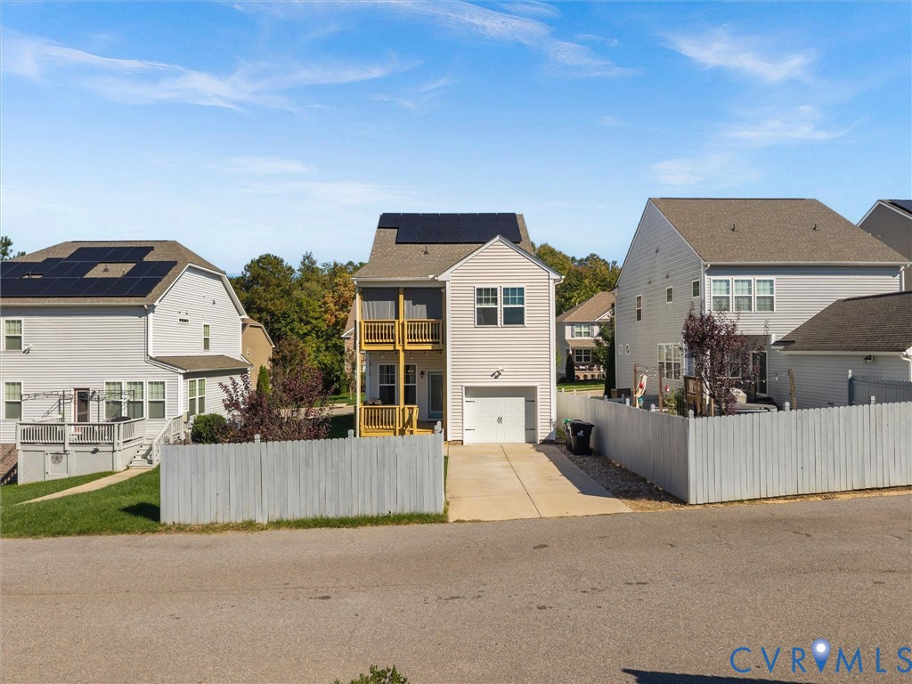 Two-story residence featuring light-colored horizontal siding, rooftop solar panels, a single-car garage, and a multi-level wood-railed deck