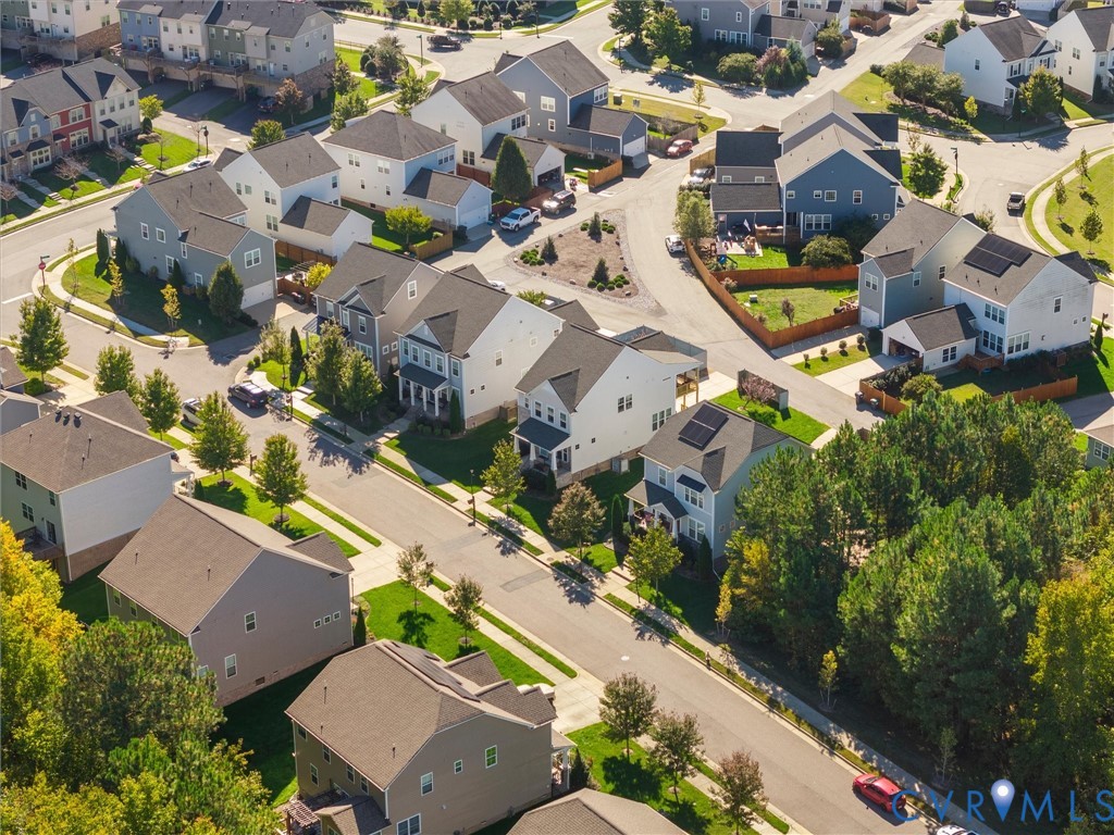 Aerial perspective of a suburban neighborhood featuring paved streets, established landscaping with mature trees, and residential properties with varied rooflines and solar panel installations
