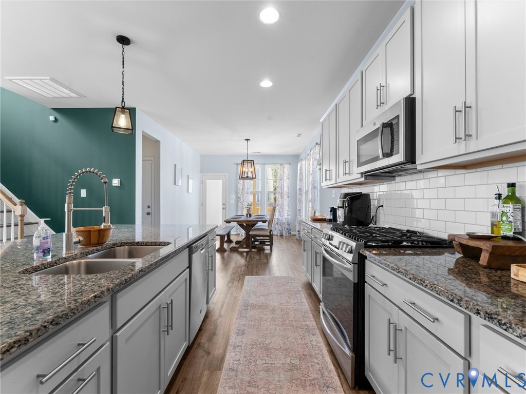 Kitchen featuring stone countertops, white shaker-style cabinetry, subway tile backsplash, stainless steel gas range, and a large center island with an undermount sink