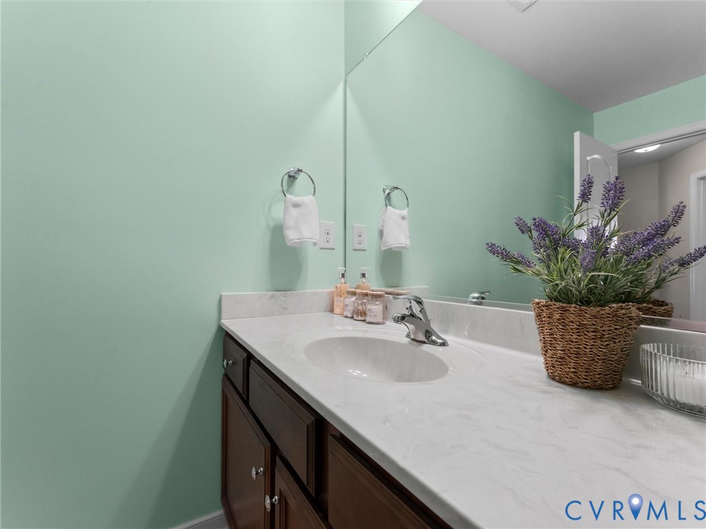 Vanity featuring dark wood cabinetry, an integrated stone-composite countertop with an oval under-mount sink, polished chrome faucet, and a large wall-mounted mirror