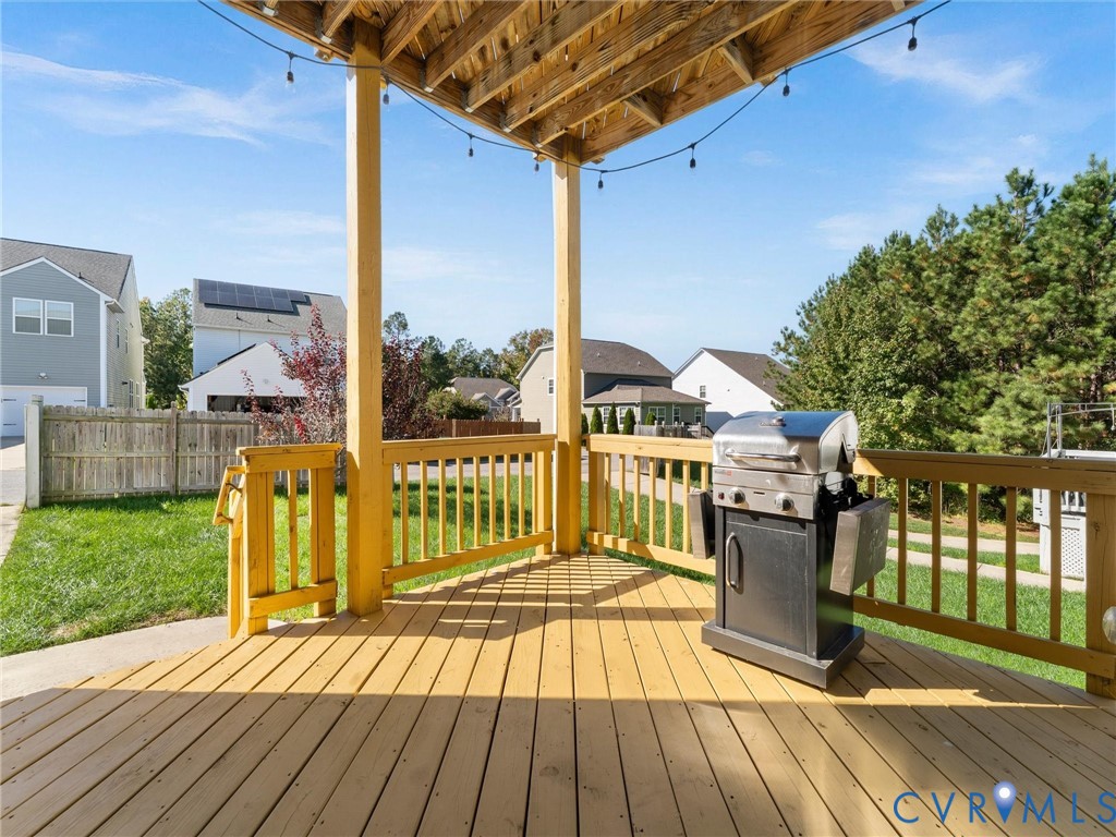 Covered wooden deck featuring natural wood-finish railings, overhead structural beams, and a concrete patio section