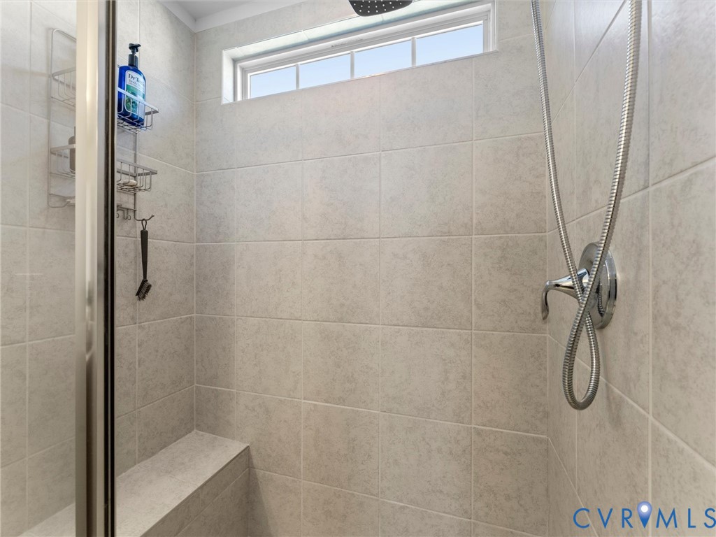 Shower enclosure featuring neutral tile wall surrounds, a built-in bench seat, a transom window, and a chrome handheld shower fixture