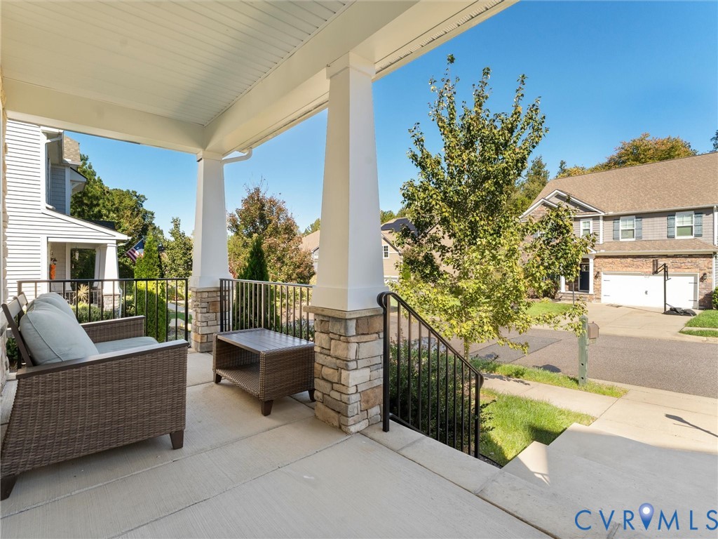 Covered front porch featuring concrete flooring, tapered columns with stone-veneer bases, and black metal railings