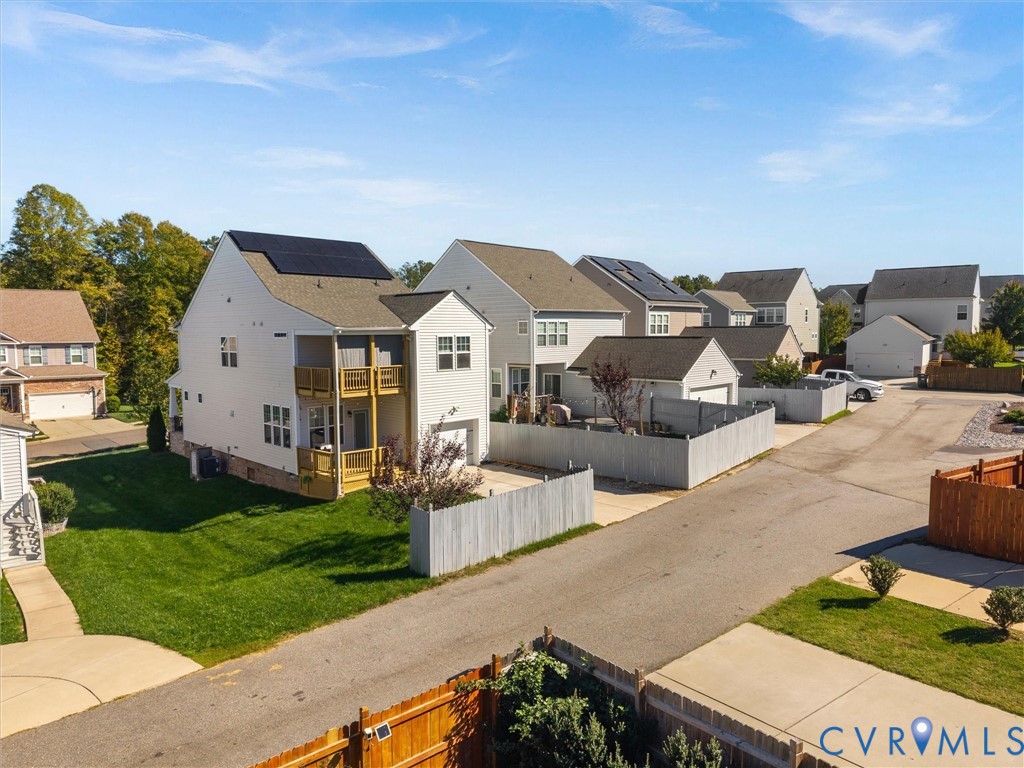 Two-story residence featuring solar panels, stacked balconies, light-colored siding, and a concrete driveway