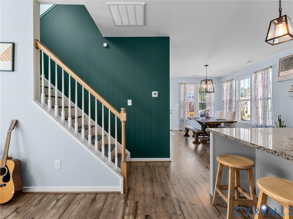 Staircase with wooden handrail and white balusters, wood-finish flooring, accent wall, and stone-surface kitchen island