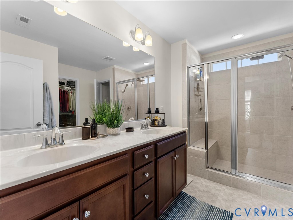 Double vanity with a stone countertop, dual undermount sinks, full-width mirror, and a glass-enclosed shower featuring tile surround and a built-in bench