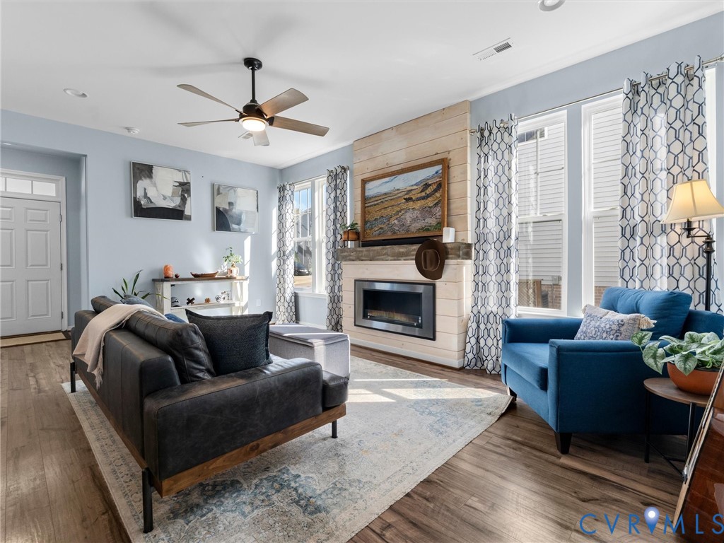 Living area featuring wood-finish flooring, a horizontal wood-plank fireplace surround, a metal-framed gas fireplace, and a ceiling-mounted fan with integrated lighting