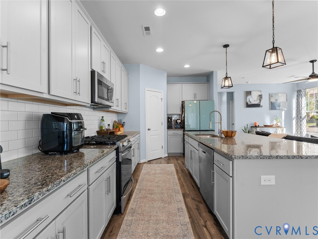 Kitchen featuring shaker-style cabinetry, stone countertops, a subway tile backsplash, stainless steel appliances, and wood-finish flooring