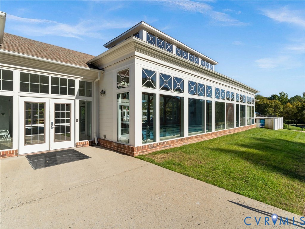 Exterior featuring expansive glass wall panels with grid detailing, clerestory windows, brick foundation base, double-door entryway, and concrete patio