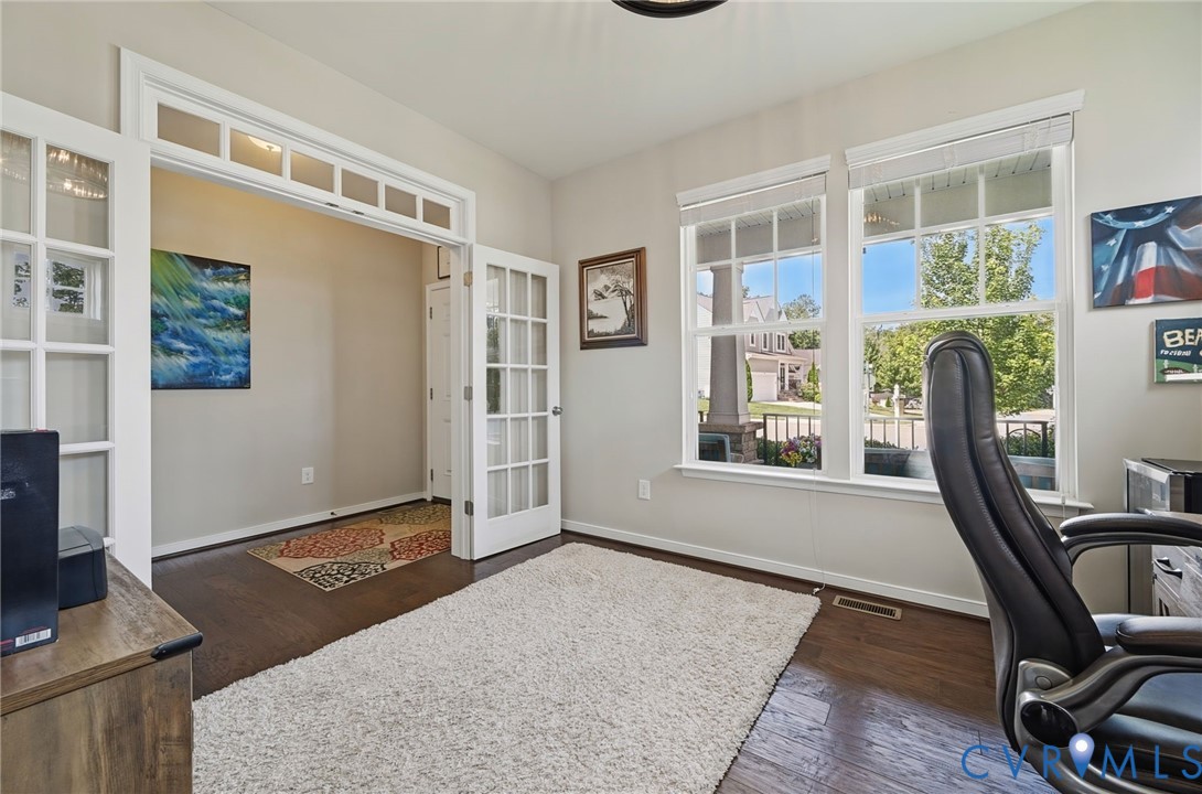 Room featuring wood-finish flooring, multi-pane French doors with transom windows, and multiple windows with white trim Room featuring wood-finish flooring, multi-pane French doors with transom windows, and multiple windows with white trim