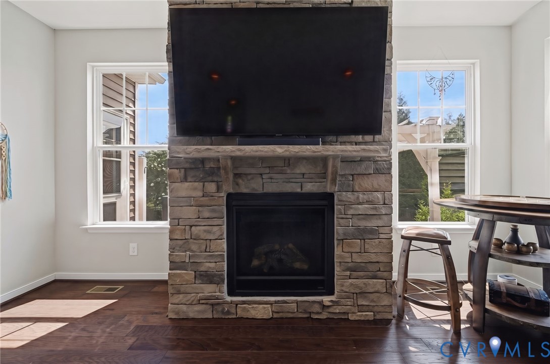 Floor-to-ceiling stone fireplace with a thick stone mantel, dual windows with grid detailing, and dark wood-finish flooring Floor-to-ceiling stone fireplace with a thick stone mantel, dual windows with grid detailing, and dark wood-finish flooring