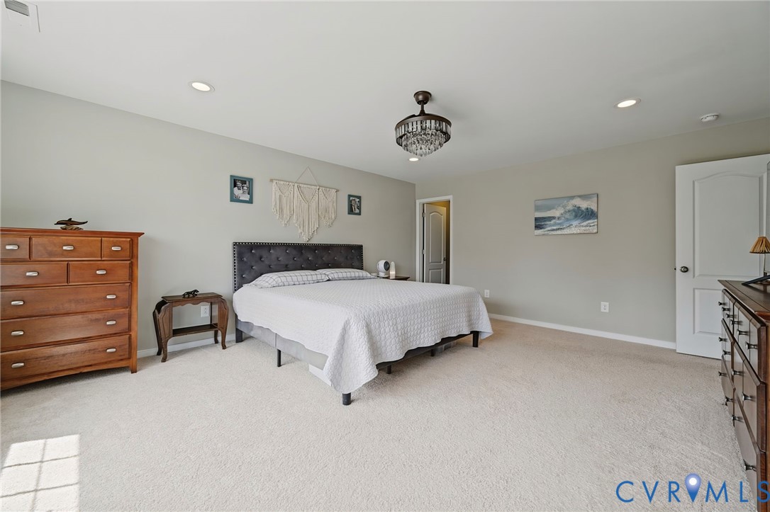 Spacious room featuring neutral carpeting, recessed lighting, a central tiered crystal light fixture, and a solid-core interior door