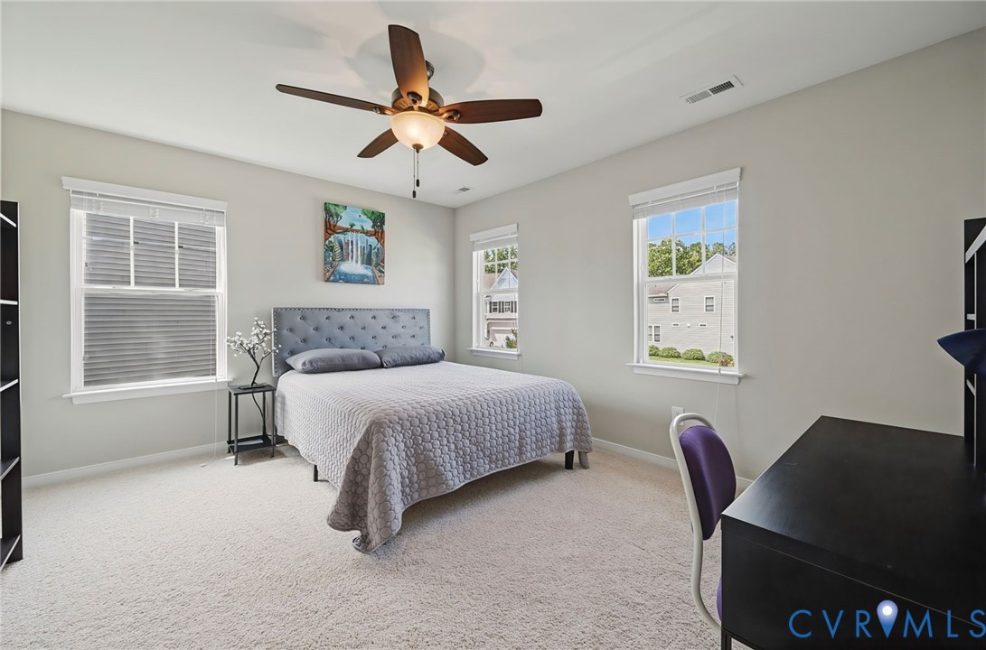Neutral-toned bedroom featuring carpeting, three windows with blinds, and a multi-blade ceiling fan with integrated lighting