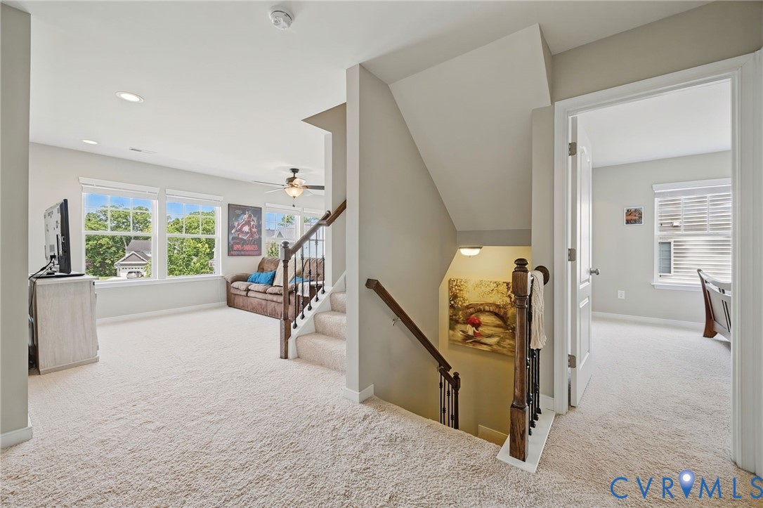 Neutral-toned interior featuring wall-to-wall carpeting, recessed lighting, double-hung windows, and a staircase with a wood handrail and metal balusters