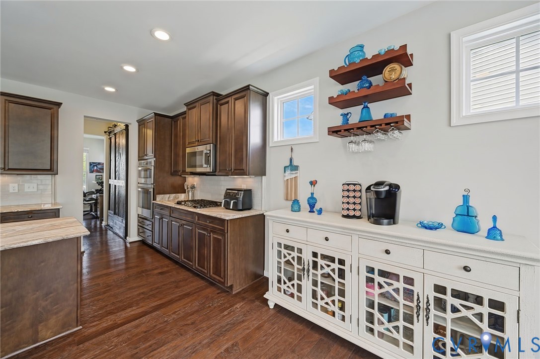Kitchen featuring dark wood-finish cabinetry, recessed lighting, hardwood flooring, wall-mounted wood shelving, and a white built-in storage console with decorative glass-panel doors