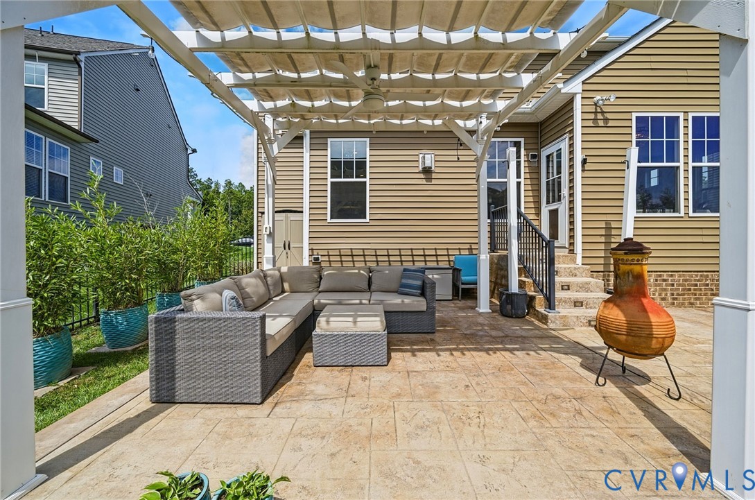 Stamped concrete patio featuring a white pergola with retractable canopy, ceiling fan, and metal railing leading to the exterior door