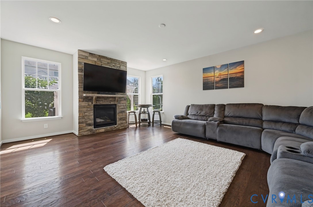 Living space featuring wood-finish flooring, recessed lighting, and a stone-veneer fireplace with a wooden mantel Living space featuring wood-finish flooring, recessed lighting, and a stone-veneer fireplace with a wooden mantel