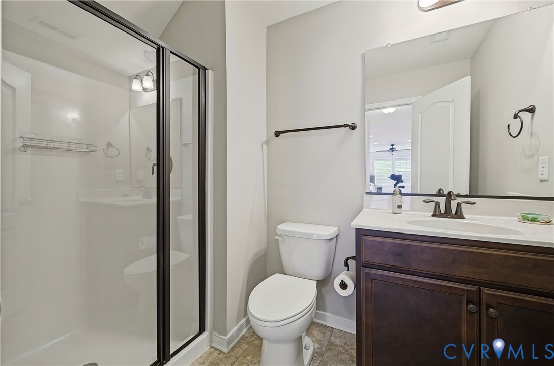 Bathroom featuring a walk-in shower with a glass enclosure, dark wood-finish cabinetry, solid-surface countertop with an integrated basin, and a wall-mounted mirror
