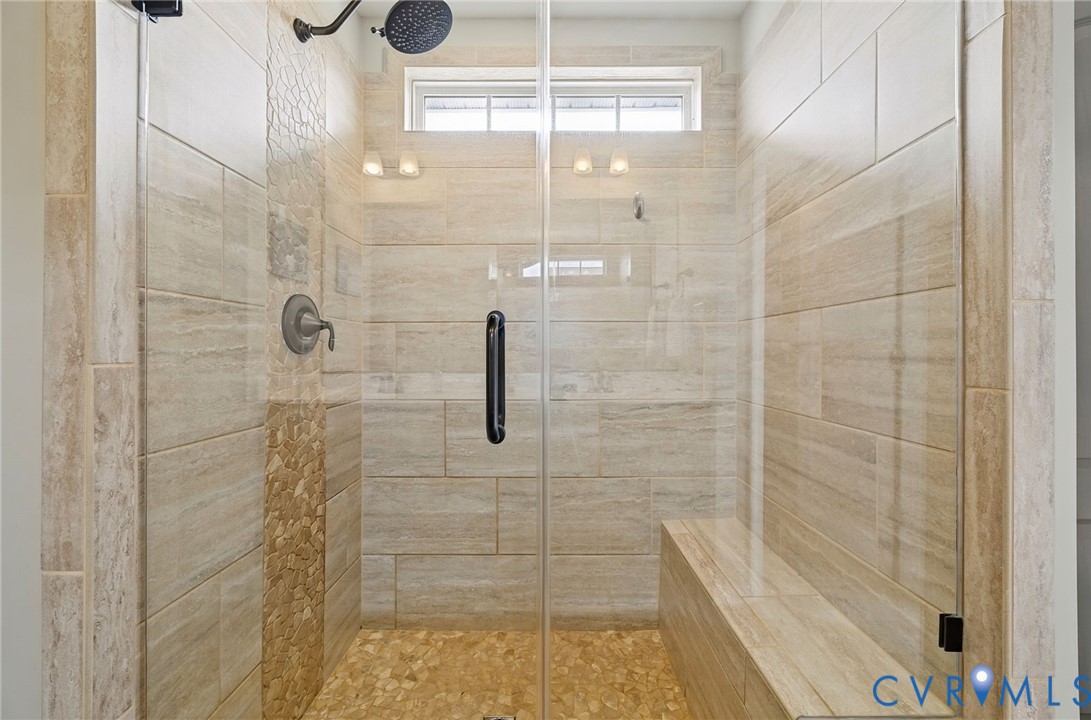Walk-in shower featuring floor-to-ceiling tile, a built-in tile bench, a frameless glass door, a stone-tiled shower floor, and a wall-mounted shower head