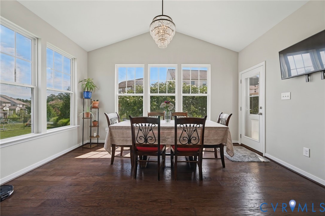 Vaulted ceiling with a central multi-tier crystal chandelier, wood-finish flooring, and expansive windows