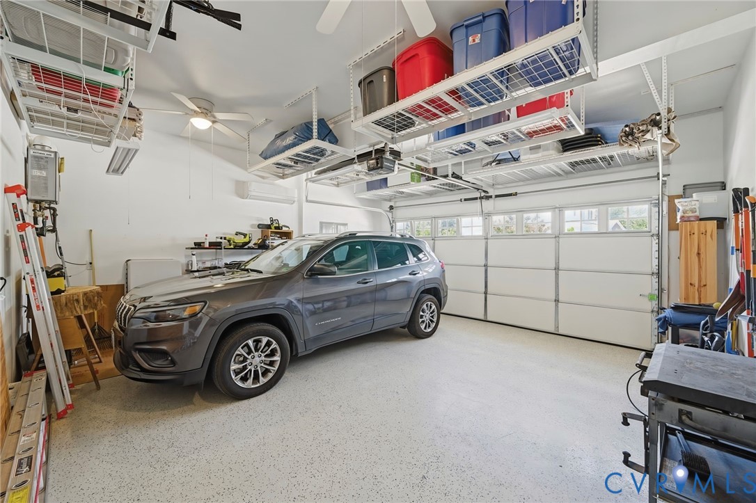 Multi-car garage featuring epoxy-coated flooring, overhead metal storage racks, wall-mounted heating and cooling unit, and sectional roll-up garage door with windows