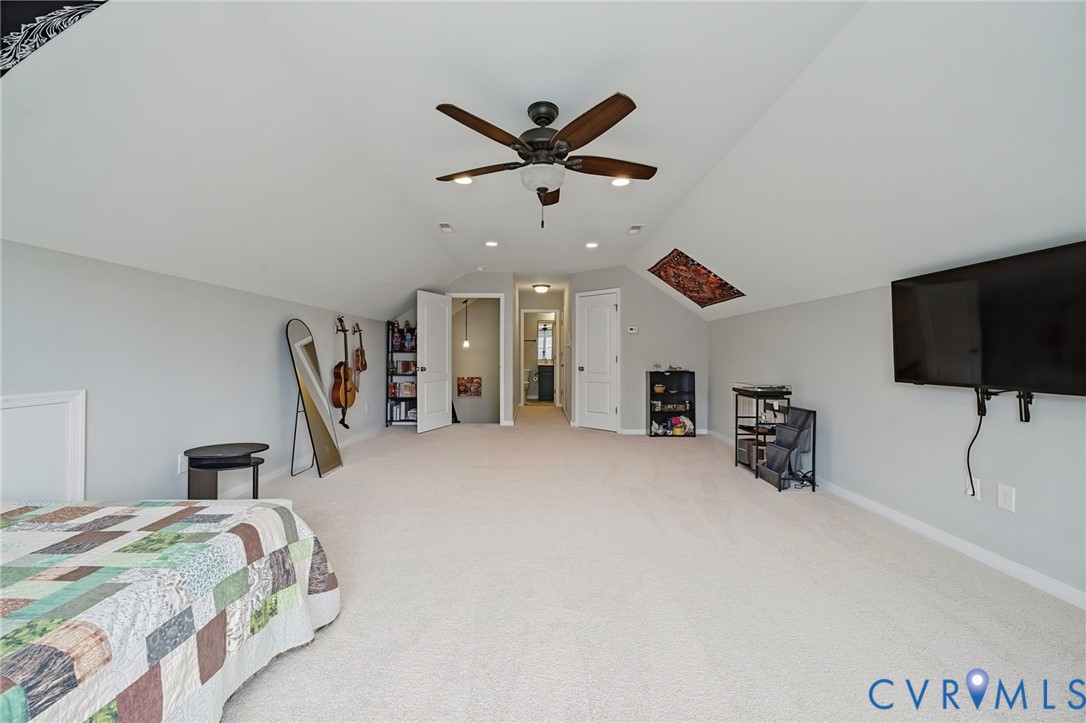 Expansive room featuring vaulted ceilings, a skylight, carpeted flooring, a ceiling fan with integrated lighting, and recessed ceiling lighting