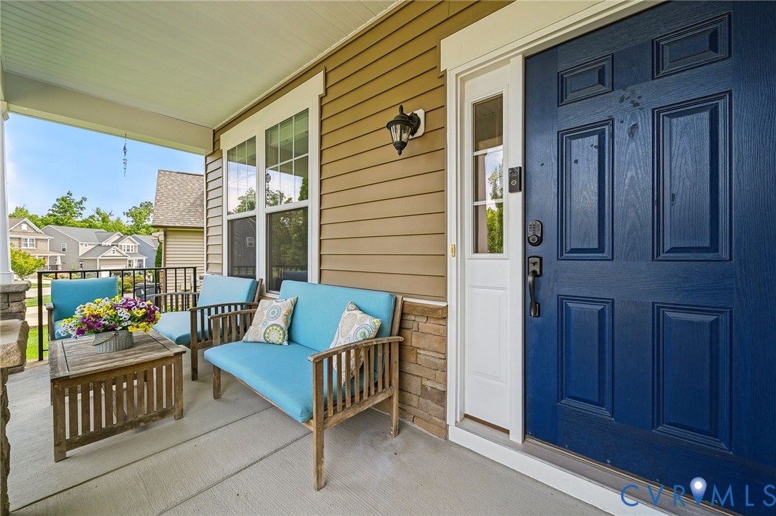 Covered front porch featuring a concrete floor, stone veneer accents, lap siding, a sidelight-equipped door, and an exterior wall-mounted light fixture Covered front porch featuring a concrete floor, stone veneer accents, lap siding, a sidelight-equipped door, and an exterior wall-mounted light fixture