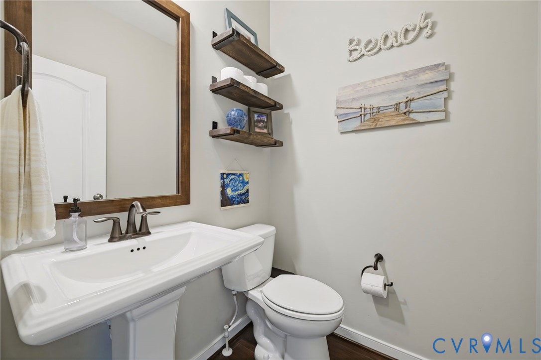 White pedestal sink with a dual-handle metal faucet, framed wood-finish mirror, and three tiered wall-mounted wood-finish shelves