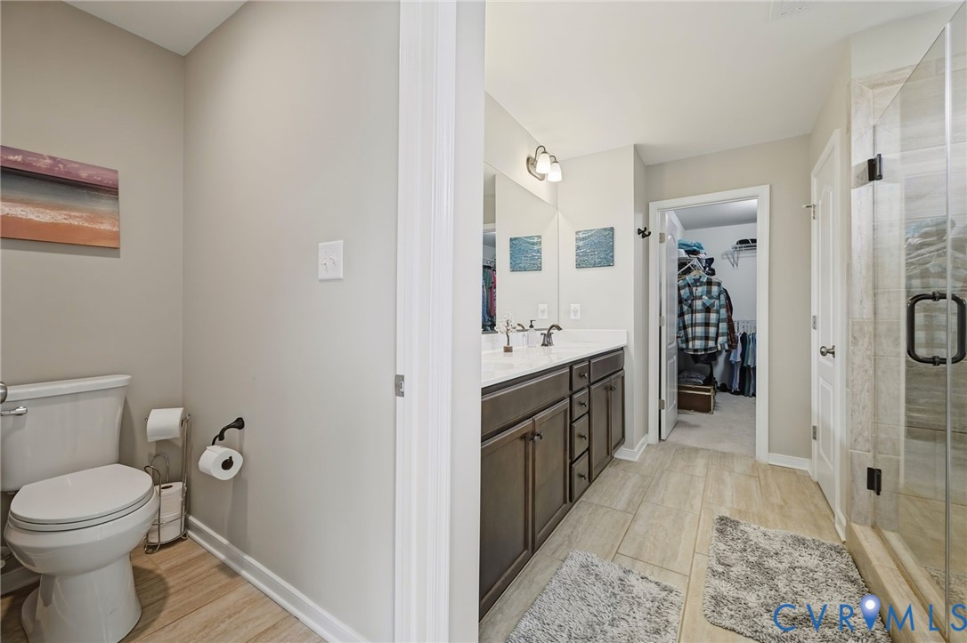 Bathroom featuring a dual-sink vanity with dark cabinetry, stone-finish countertops, tile flooring, and a walk-in glass-enclosed shower